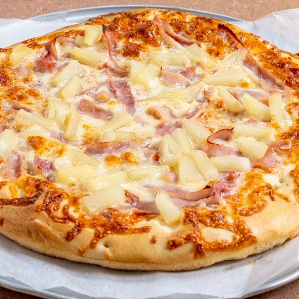 Hawaiian pizza topped with ham, pineapple, and melted cheese on a metal tray lined with parchment paper.