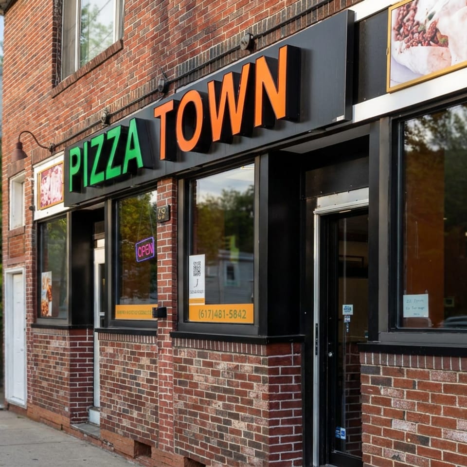 Brick storefront for Pizza Town featuring colorful signage, an open sign, pizza advertisements, and a sidewalk entrance.